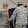 Two U.S. Army soldiers in ACU (Army Combat Uniform) are participating in a military colors ceremony, likely a change of command or casing/uncasing of colors. The soldier on the left, identified by his name tape as 'HAMMER' and wearing a Colonel's eagle insignia, is holding a guidon staff. A unit streamer reading '504th Infantry' is visible on the flag, along with campaign streamers including one labeled 'SICILY'.