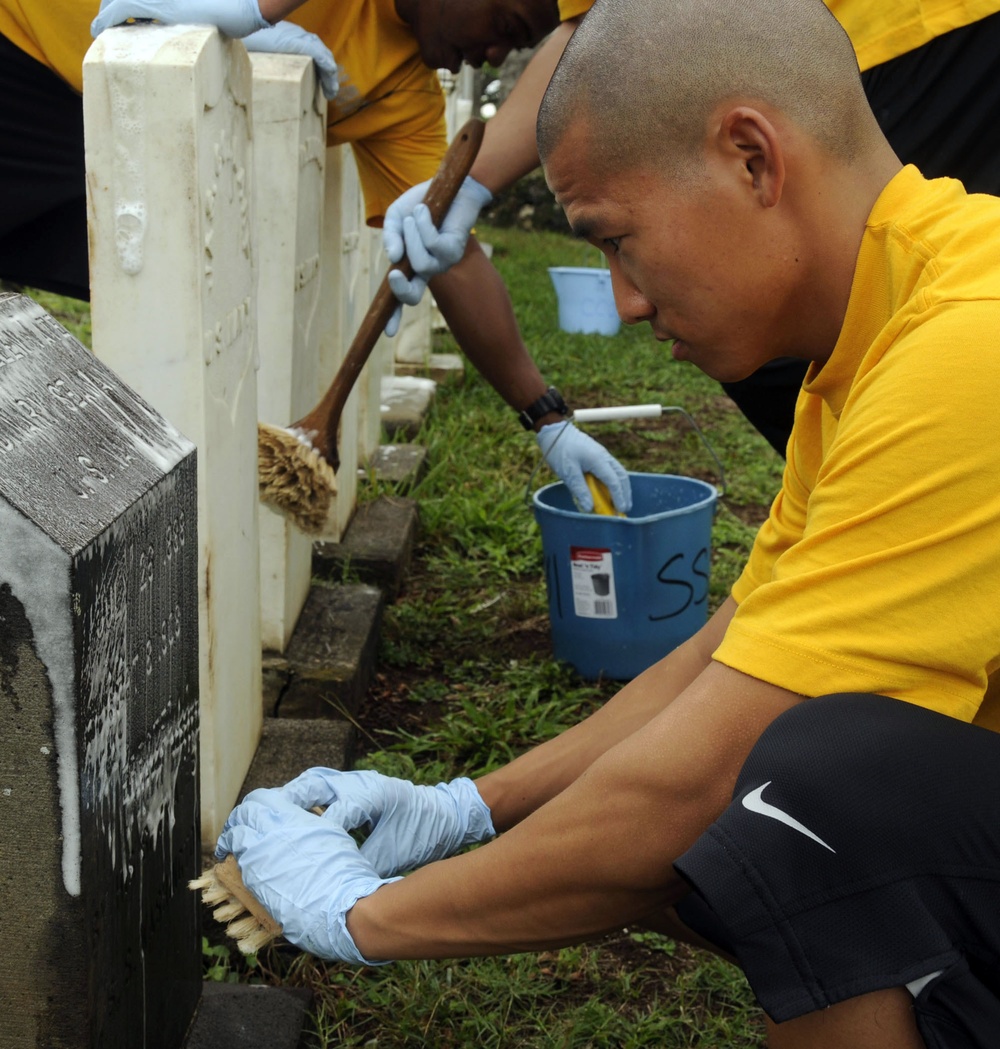 Petty Officer 2nd Class Kristopher Wee, operations specialist, assigned to the guided-missile destroyer USS Chafee, brushes a Navy headstone during a cemetery clean in preparation for Veterans Day. More than 40 Sailors assigned to Chafee and various comma