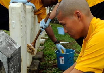 Petty Officer 2nd Class Kristopher Wee, operations specialist, assigned to the guided-missile destroyer USS Chafee, brushes a Navy headstone during a cemetery clean in preparation for Veterans Day. More than 40 Sailors assigned to Chafee and various comma