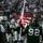 New York Jets Vs Jacksonville Jaguars Military Ceremony A New York Jets NFL player wearing jersey number 92 carries a large American flag during what appears to be a pre-game ceremony or team entrance. The player is in full green and white Jets uniform with a '50 Seasons NY' anniversary patch visible on the jersey. The stadium is filled with spectators and other Jets players are visible in the background.