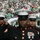 New York Jets Vs Jacksonville Jaguars Military Ceremony United States Marines in dress blues are standing at attention on a football field, with one Marine visibly saluting. The scene appears to be a pre-game or halftime military ceremony at a New York Jets NFL game, evidenced by the green Jets jerseys worn by players and fans. The stadium stands are filled with spectators, many of whom have their hands over their hearts, suggesting the National Anthem is being performed.