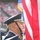New York Jets Vs Jacksonville Jaguars Military Ceremony A military color guard is presenting flags at what appears to be a large public event, likely a sporting event given the stadium crowd visible in the background. At least two uniformed service members are visible in the foreground, with the U.S. flag prominently displayed. A second flag with a blue and gold design, consistent with a U.S. Air Force flag, is partially visible in the background.