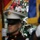 New York Jets Vs Jacksonville Jaguars Military Ceremony The image captures a scene at a New York Jets NFL game, featuring a U.S. Marine in dress uniform with a cover (hat) in the foreground, likely part of a color guard ceremony. A Jets player wearing jersey number 26 and a white helmet with the Jets logo is visible in the background. Colorful flags and stadium spectators are also visible in the background.