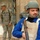 217th Military Police train Iraqi police at the Criminal Justice Center The image shows a foreground figure wearing a blue uniform, tan body armor labeled 'Survival Armor,' a helmet, and holding a wooden-stocked firearm, identified by a patch as Iraqi Police (IP). In the background, two individuals in US military ACU (Army Combat Uniform) camouflage pattern are visible near a building with a metal gate. The scene appears to depict a joint security or patrol operation.