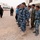 Alaskan MPs run Iraqi Police through tough training The image shows a group of military and law enforcement personnel standing in formation on a gravel compound. Multiple uniform types are visible, including blue camouflage, olive/woodland camouflage, and black uniforms, suggesting a multi-unit or joint inspection scenario. A senior officer in distinctive camouflage with a red beret appears to be conducting a review or inspection of the assembled personnel.