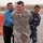 Alaskan MPs run Iraqi Police through tough training A U.S. Army Military Police soldier named Eliason is shown smiling in a friendly interaction with what appears to be an Iraqi Ministry of Interior police officer and a civilian. The scene takes place at what appears to be a forward operating base or checkpoint, identifiable by concrete barriers, gravel ground, and perimeter walls. The atmosphere appears relaxed and cooperative, suggesting a joint operations or liaison context.