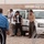 Alaskan MPs run Iraqi Police through tough training The image shows a group of men standing near a white SUV/vehicle in what appears to be a dusty, arid environment consistent with a Middle Eastern setting. Razor wire (concertina wire) is visible in the foreground, suggesting a security checkpoint or controlled perimeter. Several men appear to be engaged in conversation near the vehicle.