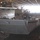 A military landing craft bearing the hull number 1680 is positioned inside what appears to be the well deck of a large amphibious assault ship or dock landing ship. The craft is floating on dark water within the enclosed bay, with the open stern gate of the host vessel visible in the background allowing bright exterior light to flood in. The scene depicts a typical well deck operation used for deploying or recovering landing craft.