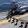 A group of U.S. Marines are boarding a CH-46 Sea Knight tandem-rotor helicopter on the flight deck of a naval vessel at sea. The helicopter bears 'MARINES' markings and the tail code 'YD' with number '3318' visible. Personnel carrying tactical gear and backpacks are walking in a line toward the rear ramp of the aircraft.