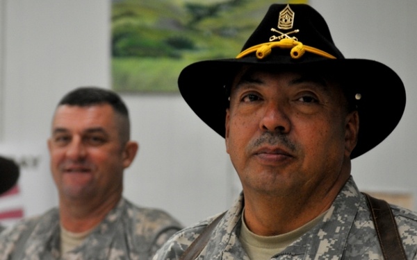 Three U.S. Army soldiers in ACU (Army Combat Uniform) digital camouflage are standing in an indoor setting. The foreground soldier, identified by name tape as 'CORDOVA,' wears a black cavalry Stetson hat with brass insignia and a Sergeant Major rank insignia on his chest. Two other soldiers are visible in the background, one also wearing a campaign-style hat.