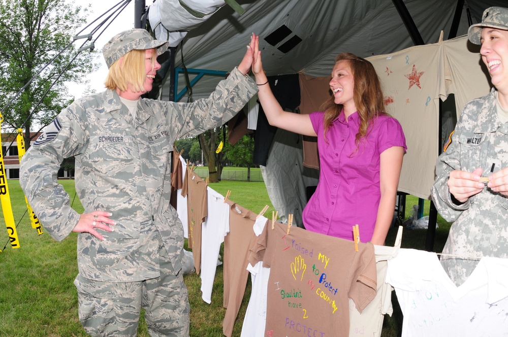 Senior Master Sgt. Susan Schroeder, left, gives a high five to Staff Sgt. Heather Prigge, both of the 119th Wing, as they hang a t-shirt on a clothesline project display, July 29, on the Fargo, N.D. Veteran's Administration Hospital grounds. The Clothesli