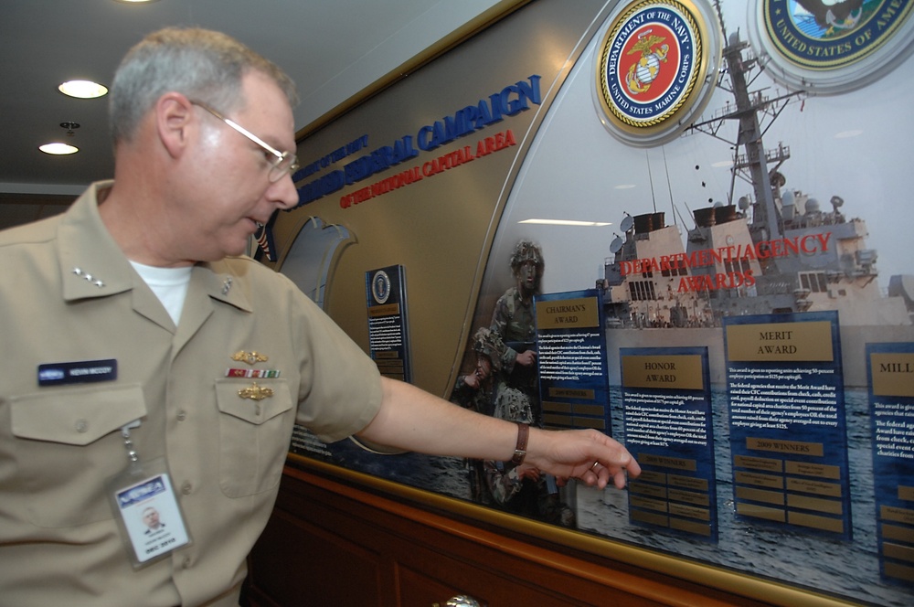 Naval Sea Systems Command Commander, Vice Adm. Kevin McCoy, points to his command’s name on a plaque listing commands that met or exceed significant fundraising goals during previous years on behalf of the Combined Federal Campaign