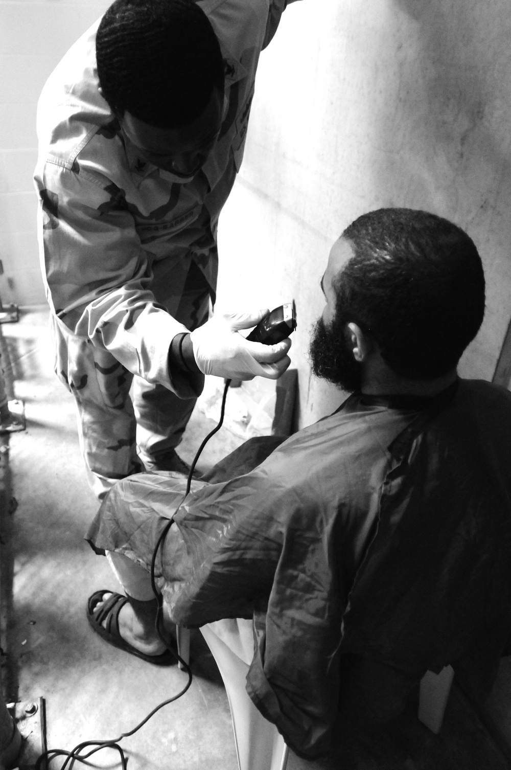 Ship’s Serviceman 3rd Class Darold Johnsonbrown trims a detainee’s beard in Camp VI.