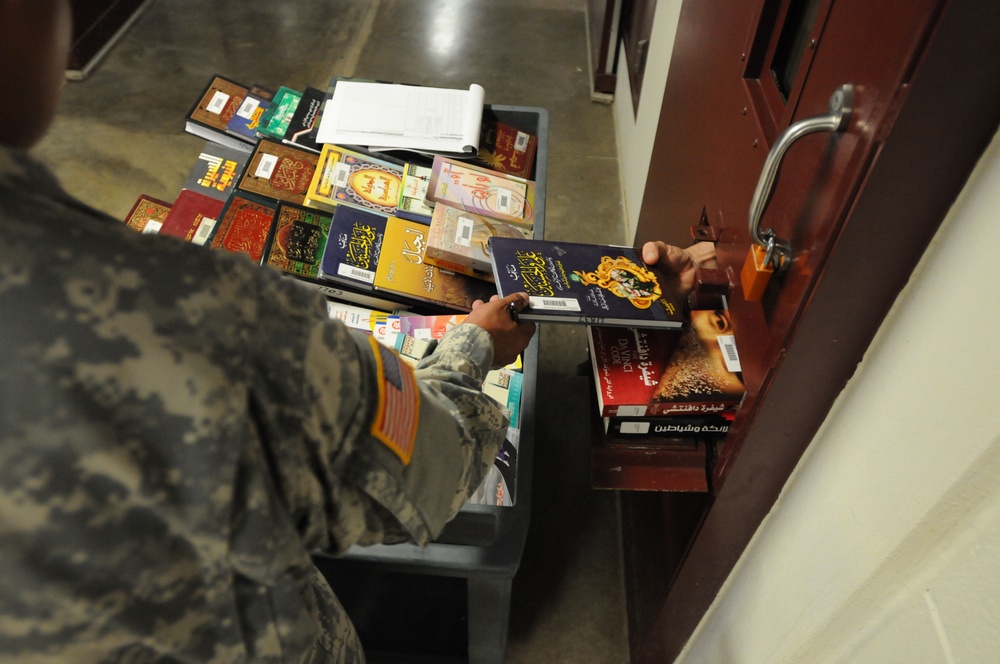 A soldier from the detainee library hands a book to a detainee in Camp Five