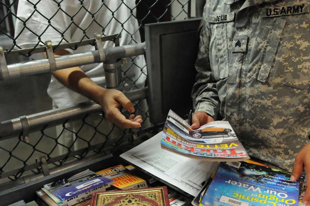 A soldier from the detainee library hands a periodical to a detainee in Camp Five