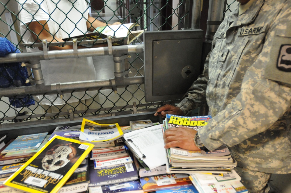 A detainee looks through a book offered to him from a Soldier from the detainee library in Camp Five