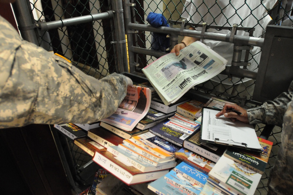 A detainee takes a newspaper given to him from a guard in Camp Five