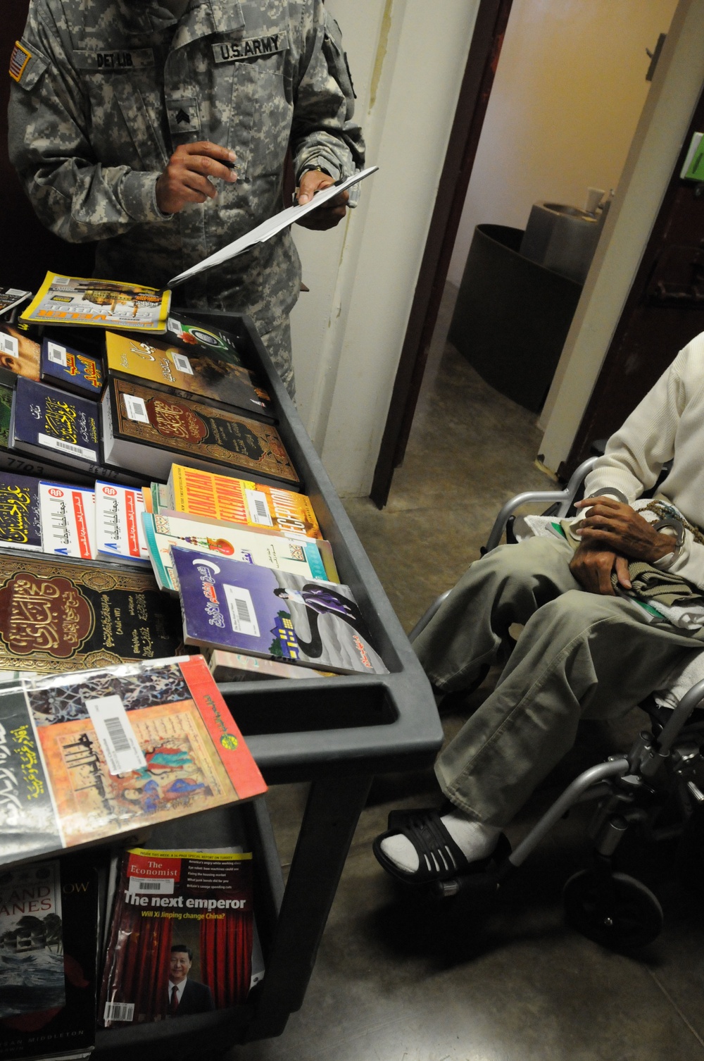 A soldier from the detainee library reviews a book record before offering books to a detainee in Camp Five