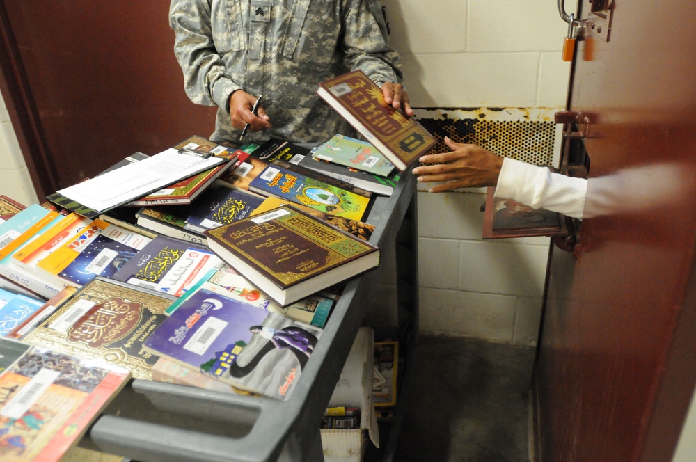 A soldier from the detainee library hands a book to a detainee in Camp Five,