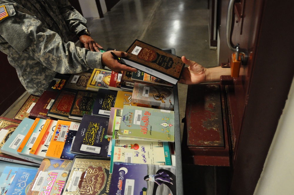 A soldier from the detainee library hands a book to a detainee in Camp Five