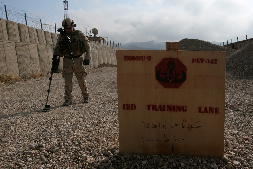 A US Navy EOD technician simulate training on how to identify possible signs of IEDs on their training lane at Camp Griffin