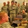 432nd Civil Affairs Battalion prepares for deployment to Afghanistan A group of U.S. Army soldiers in ACU (Army Combat Uniform) are gathered in what appears to be a classroom or training room. A soldier in the foreground is seated with what appears to be a nasopharyngeal airway (NPA) or similar medical training device inserted in his nostril, suggesting a medical training demonstration. The group of approximately 15 soldiers standing in the background appear to be observing and reacting with smiles and laughter.