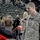 432nd CA BN prepares for deployment to Afghanistan A Fox News reporter is interviewing a U.S. Army soldier in ACU (Army Combat Uniform) inside what appears to be an indoor arena or stadium. The soldier, who wears an Airborne patch and corporal rank insignia, is smiling and speaking into the microphone. The setting suggests a military homecoming or public event, with civilians and sparse audience members visible in the background.