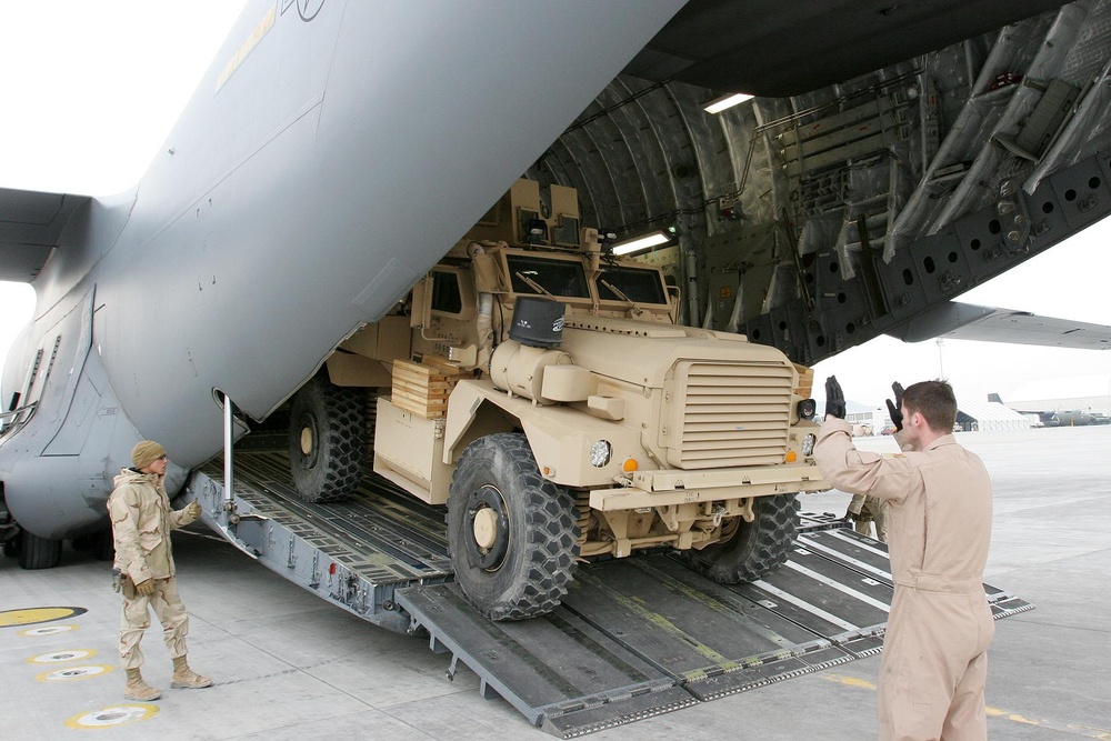 A US Air Force aircrewman loads a truck into a C-17 aircraft