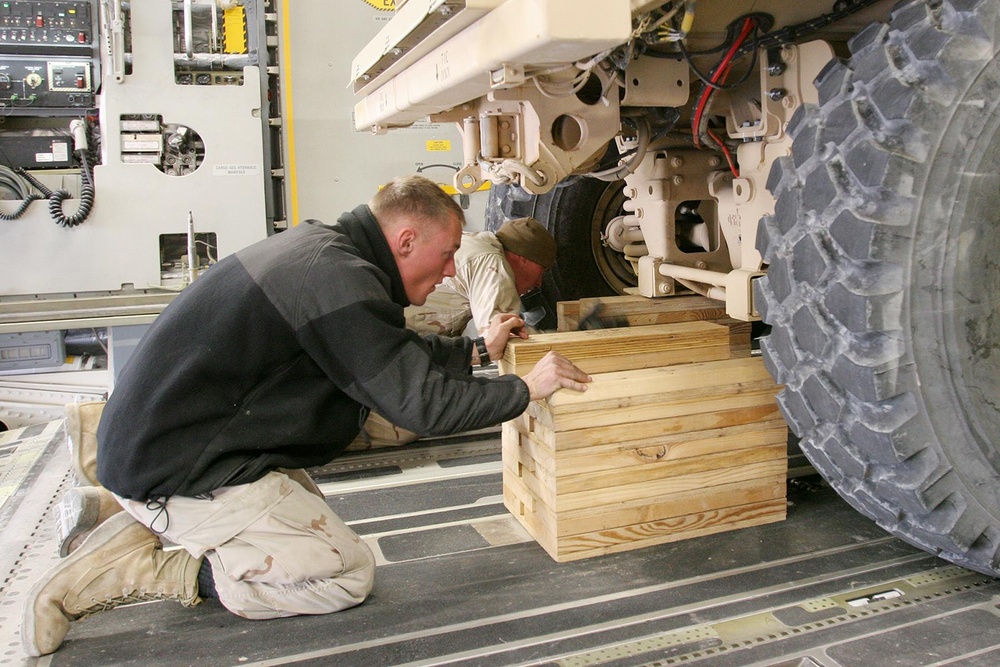 Seabees secure a truck onboard a C-17 aircraft for transport