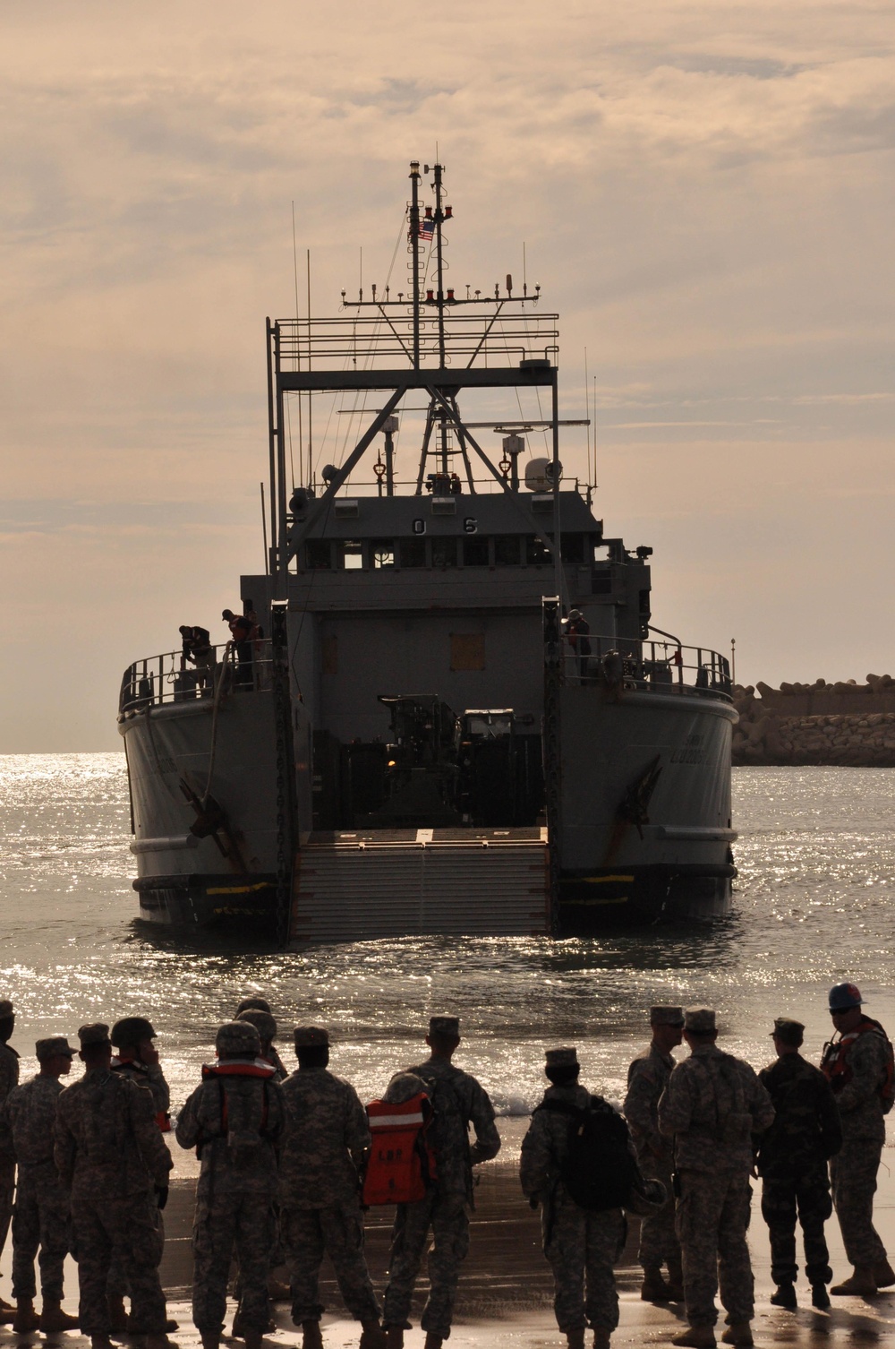 Service members watch as U.S. Army vessel Landing Craft Utility 2006