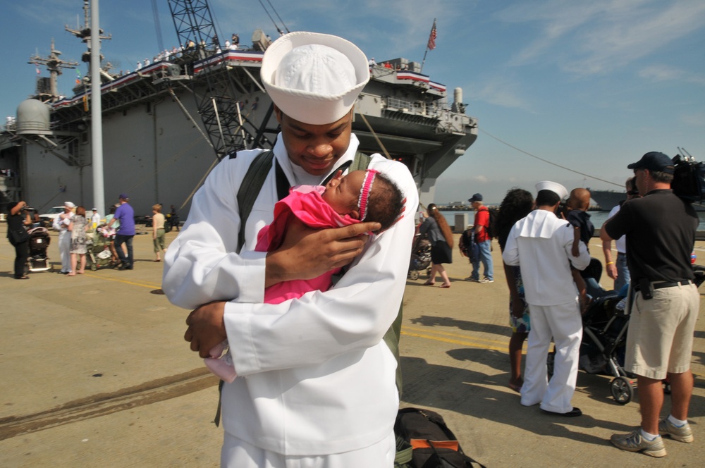 Seaman Demontay Blue holds his daughter for the first time during the amphibious assault ship USS Kearsarge return to Naval Station Norfolk
