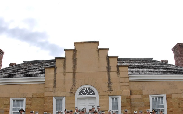 A large group of military personnel in U.S. Army ACU (Army Combat Uniform) digital camouflage are posed for a formal group photograph in front of a historic sandstone building. The building features colonial or early American architectural style with brick chimneys, a fanlight doorway, and symmetrical window placement. The photo appears to be taken at a historic site, possibly a national park or landmark.