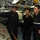 USS Thach sailors explains console to Chilean naval officers Three naval personnel are gathered inside what appears to be a ship's control or engineering room. A US Navy sailor wearing a dark cap is pointing at a control panel while briefing or instructing two other individuals, one of whom wears a Chilean Navy flag patch and a name tag reading 'USS THACH'. This appears to be an exchange or liaison visit between US and Chilean naval personnel aboard a US Navy vessel.