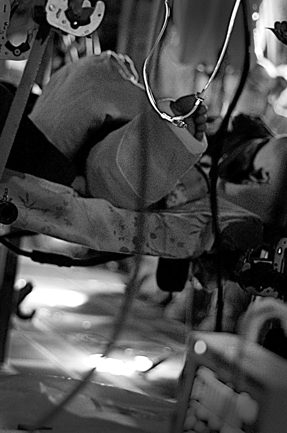 A black and white photograph showing what appears to be a medical evacuation or casualty transport scenario, likely inside a military helicopter or aircraft. A person is lying on a litter/stretcher and appears to be receiving medical care, with visible medical tubing and equipment. The image is rotated or taken at an unusual angle, and motion blur suggests the vehicle is in transit.