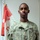 A U.S. Army soldier named Ephraim poses for a formal portrait photo indoors. He is wearing the Army Combat Uniform (ACU) with digital camouflage pattern. A red and white military guidon flag is visible in the background.