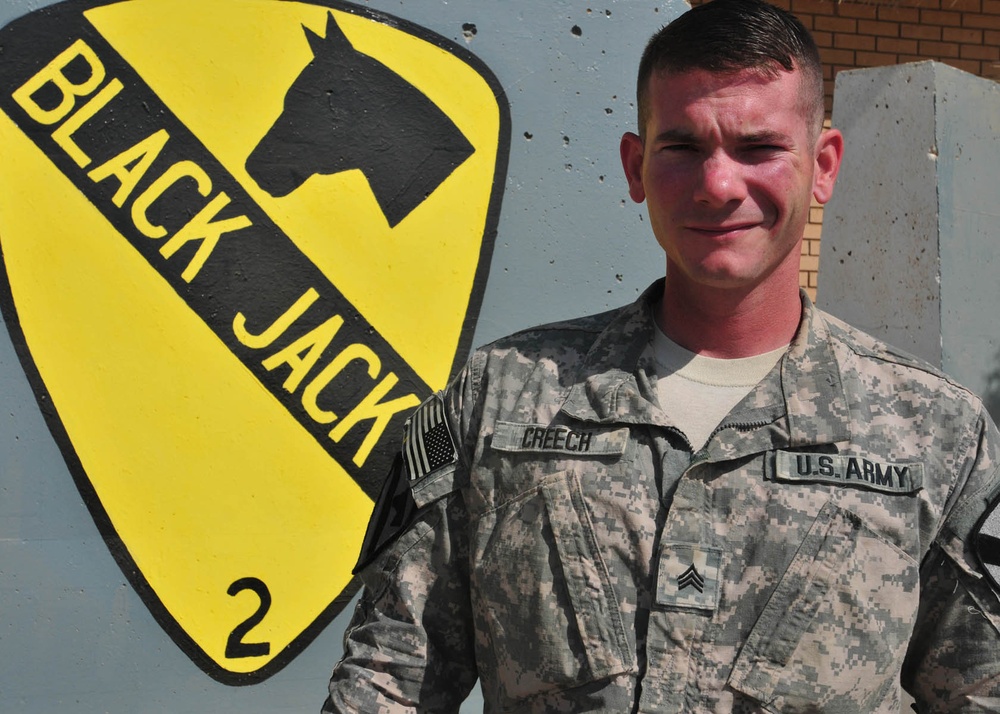 Soldier stands in front of unit crest while serving on a deployment to Iraq
