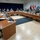 New SACEUR makes first visit to Kosovo A formal multinational military conference or briefing is taking place in a large meeting room arranged in a U-shaped table configuration. Numerous military personnel in various national uniforms are seated around the tables, along with at least one civilian in a dark suit. Multiple national flags are displayed along the back wall, indicating a multinational or coalition military gathering.