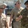 New SACEUR makes first visit to Kosovo The image shows a group of military personnel walking together, appearing to be engaged in conversation. The foreground features a US Navy officer wearing a garrison cap with four-star insignia and an Italian Army officer in camouflage uniform with a black beret. The setting appears to be an outdoor military installation or base.