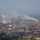 New SACEUR makes first visit to Kosovo An aerial view of a large industrial complex, likely a coal-fired power plant or steel facility, situated adjacent to a residential town. Multiple smokestacks and at least one cooling tower are actively emitting smoke and steam into a hazy atmosphere. Large stockpiles of what appears to be coal are visible in the foreground of the industrial area.