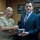 New SACEUR makes first visit to Kosovo Two men are posing together while jointly holding a silver ceremonial bowl, suggesting a formal presentation or gift exchange. One man is wearing a military uniform with rank insignia and service ribbons, while the other is dressed in a civilian business suit with a striped tie. The setting appears to be an office with wood-paneled walls and framed landscape photographs.