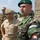 New SACEUR makes first visit to Kosovo The image shows a group of military personnel from multiple nations gathered outdoors near a stone structure. The foreground features a Slovak Army officer (name tag 'LUDVIK') wearing a green beret with three stars, alongside a US Navy/Marine officer in tan service uniform with four-star insignia, and an Italian Army officer visible in the background. The setting appears to be an official multinational military visit or ceremony.