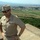 New SACEUR makes first visit to Kosovo A U.S. Navy officer in khaki service uniform stands on an elevated stone structure overlooking a rural valley with fields, trees, and a small town in the background. He is wearing a garrison cap with a Navy insignia, sunglasses, and displays multiple rank insignia and service ribbons on his uniform. The setting appears to be an outdoor overlook or fortification in a European-style landscape.