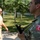 New SACEUR makes first visit to Kosovo The image shows two military personnel in an outdoor setting with trees and grass in the background. The foreground soldier is wearing Turkish Armed Forces digital camouflage uniform with a clearly visible 'TÜRKİYE' patch featuring the Turkish crescent and star flag emblem, and is carrying a weapon. A second soldier in tan/khaki uniform with sunglasses is visible in the blurred background.