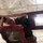 A person wearing military-style camouflage trousers and a green t-shirt is working on or handling a wooden ladder or frame structure while standing on a red metal step ladder. The photo is taken from a low angle looking upward, creating a dramatic perspective. The setting appears to be inside a large industrial or military hangar with a truss ceiling.