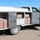 Operation Pipeline Express drug arrests A white work truck with a service body/utility bed has its compartment doors open, revealing multiple brown-wrapped rectangular bundles packed inside the storage bays. The vehicle displays signage indicating an AC and roofing business with a phone number. This appears to be a law enforcement interdiction photograph documenting contraband concealed within a commercial work vehicle.