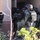 Operation Pipeline Express Drug Arrests A tactical law enforcement team in full gear is conducting what appears to be a dynamic entry or raid on a residential building. Multiple officers wearing helmets, body armor labeled 'POLICE', and tactical vests are stacked near a doorway. At least one officer's patch is consistent with DHS/CBP insignia, suggesting a federal law enforcement presence.