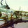 A shirtless young man stands on what appears to be an aircraft carrier flight deck in front of a U.S. Navy attack aircraft marked with the number '414'. The aircraft displays U.S. military insignia (roundel), warning labels including 'JET DANGER' and 'INTAKE', and is loaded with what appear to be ordnance/bombs on underwing pylons. The photo appears to be from the Vietnam War era based on color saturation, film quality, and aircraft type.