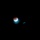 The image shows a lunar eclipse captured against a completely dark night sky. The moon displays a partial eclipse with a reddish-orange (blood moon) coloration on the upper portion and a bright white crescent on the lower left, indicating Earth's shadow partially covering the lunar surface. A smaller, dimmer secondary object — likely an optical artifact, lens flare, or a nearby celestial body — is visible to the right of the moon.