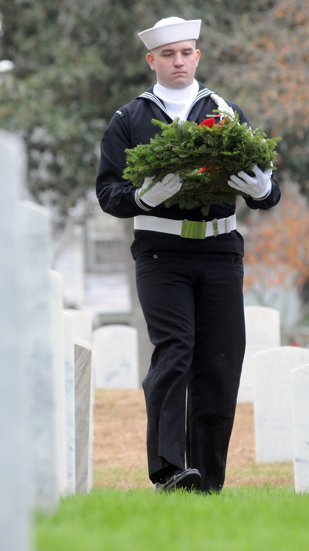 Sailor carries wreath in cemetery