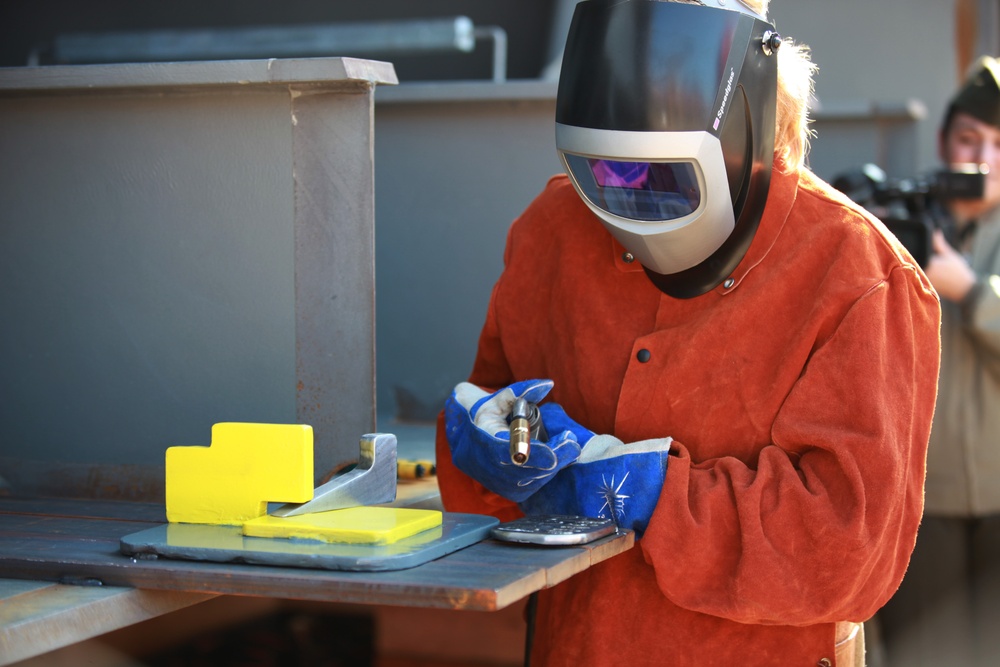 Honorary guest Pat Mills brands her initials into the Department of the Navy's newest mobile landing platform